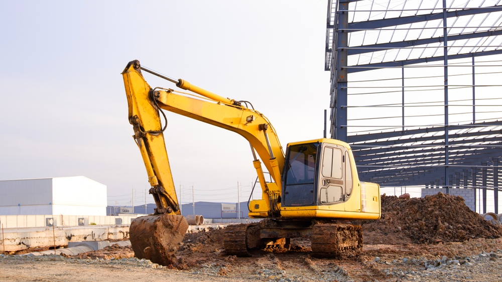 A yellow excavator digging on a construction site beside a partially built steel-framed structure.
