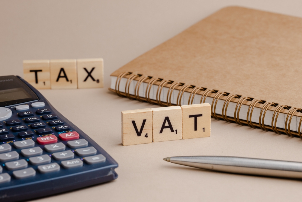 Calculator, notebook and wooden blocks spelling “tax” and “VAT”, representing tax payments and business cashflow planning