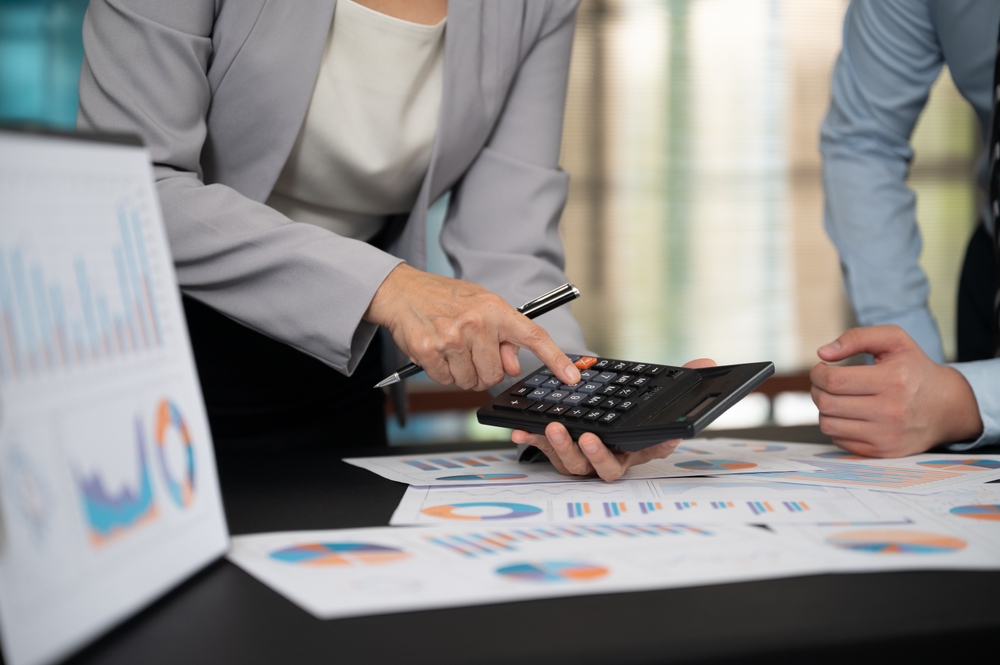 Close-up of two professionals reviewing financial charts and using a calculator to analyse business data and borrowing costs.