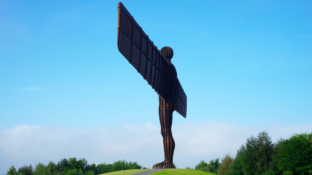 The Angel of the North sculpture standing on a grassy hill beneath a clear blue sky in Gateshead, representing the North East of England.